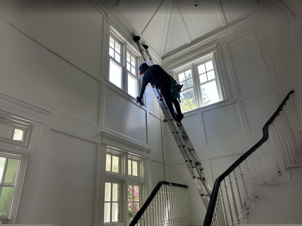 Skybleu technician on ladder cleaning high interior windows in a luxury home in San Mateo, California