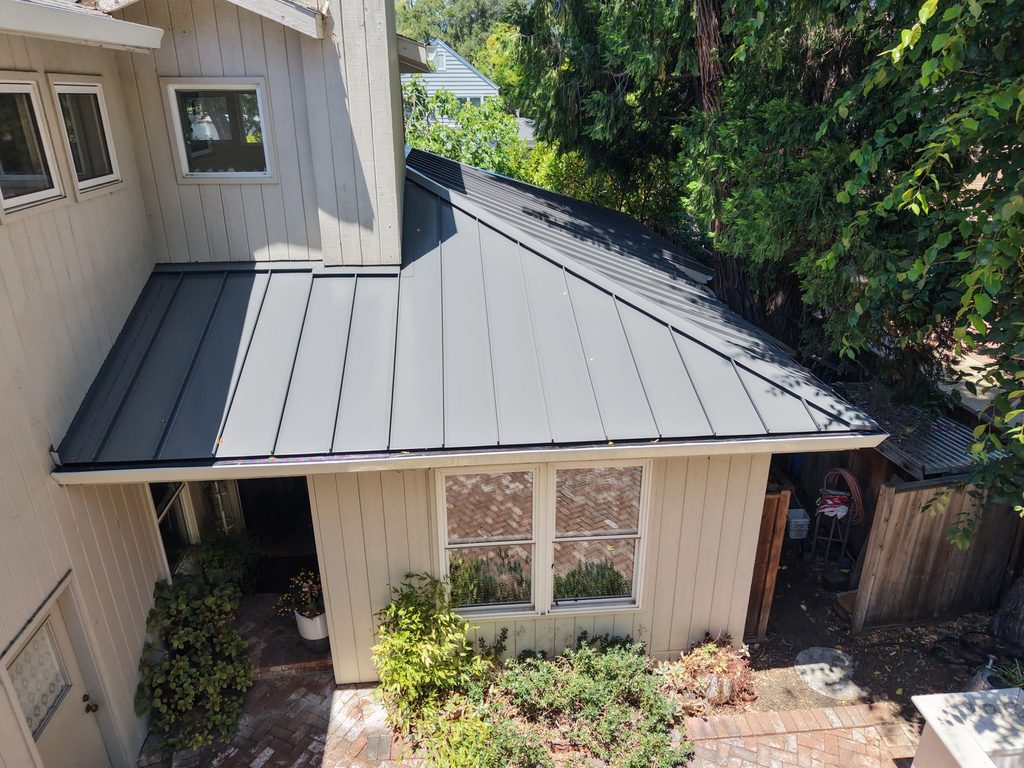 Charcoal flat-panel metal roof over a garden entry, with a brick patio and planting below