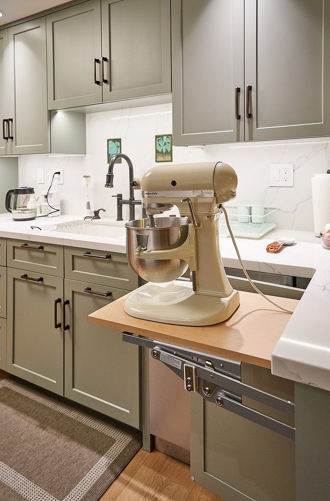 Hidden lift shelf raising a stand mixer to counter height inside a green shaker kitchen cabinet