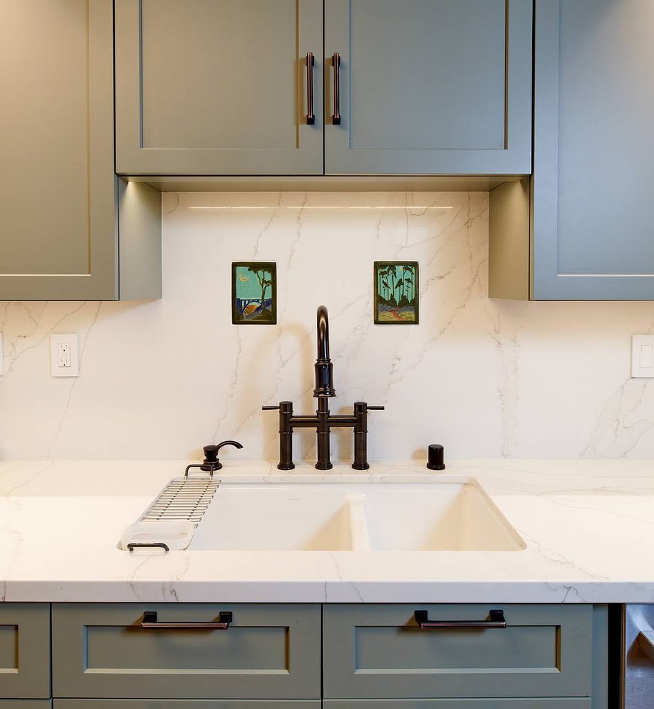 Undermount double-basin sink with a bronze bridge faucet and a quartz slab backsplash with soft grey veining